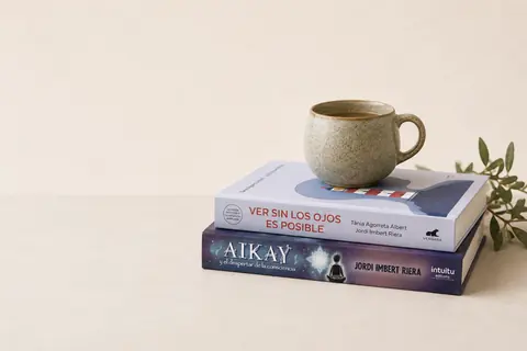 Los libros «Ver sin los ojos es posible» y «Aikay» con una taza y una rama de olivo
