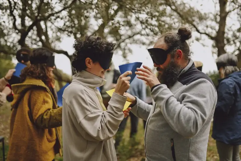 Dos personas con antifaz practicando visión intuitiva con cartulinas de colores, al aire libre entre encinas