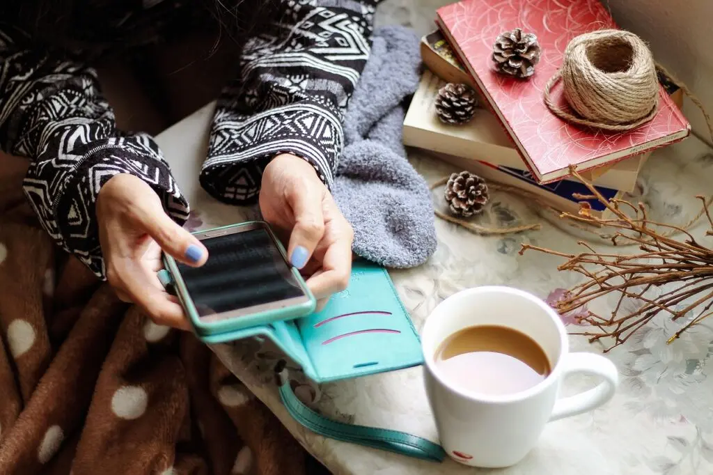 Manos sosteniendo un cuaderno sobre una manta, junto a una taza de té